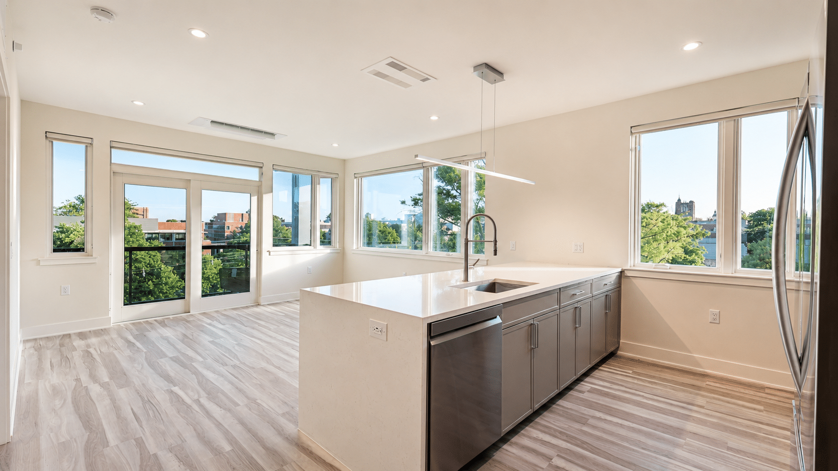 Bright open-plan apartment with a kitchen island, stainless appliances, hardwood floors, and oversized windows.