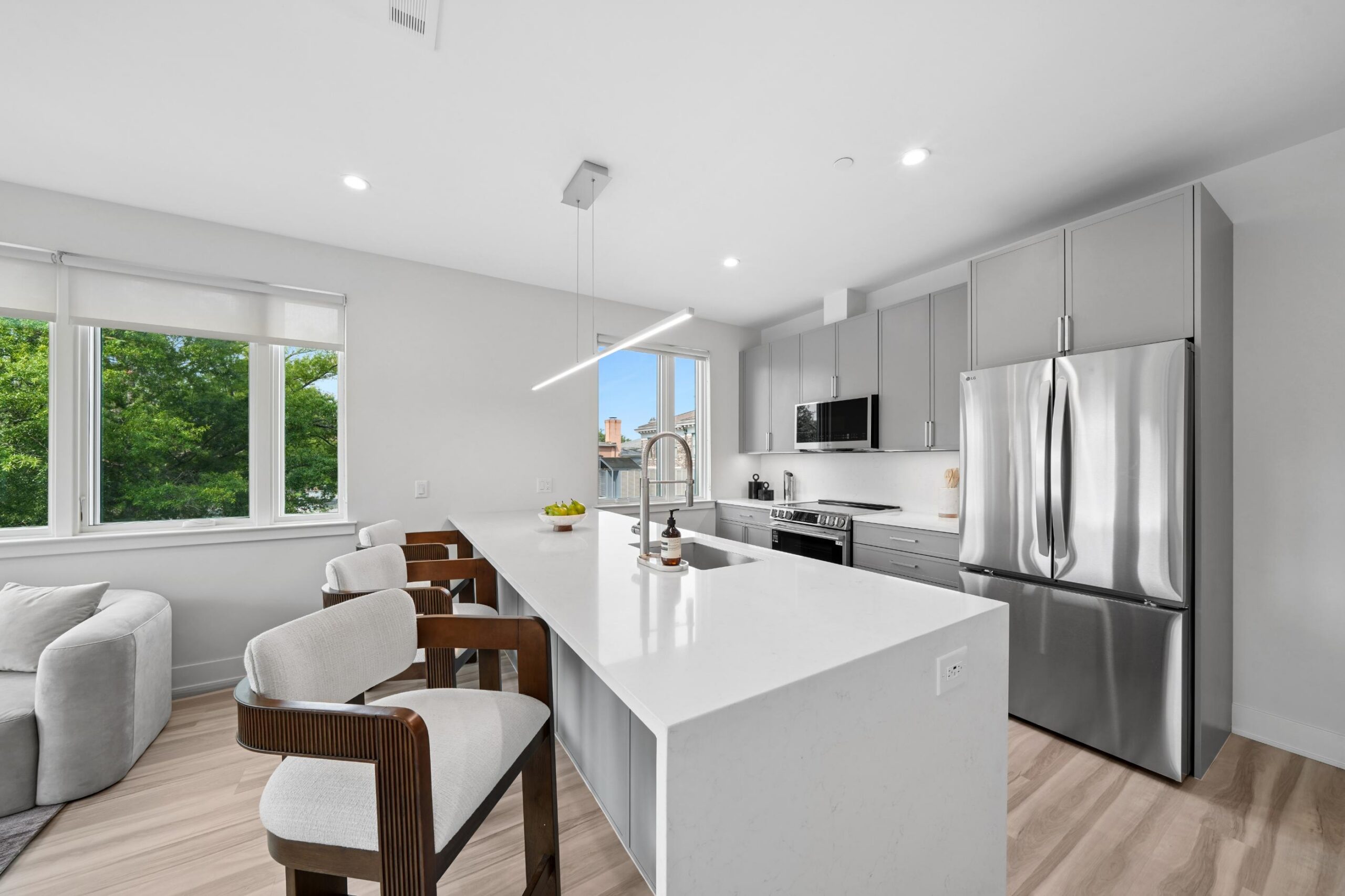 Angled kitchen area with grey cabinets and while details. 3 bar stools by kitchen island