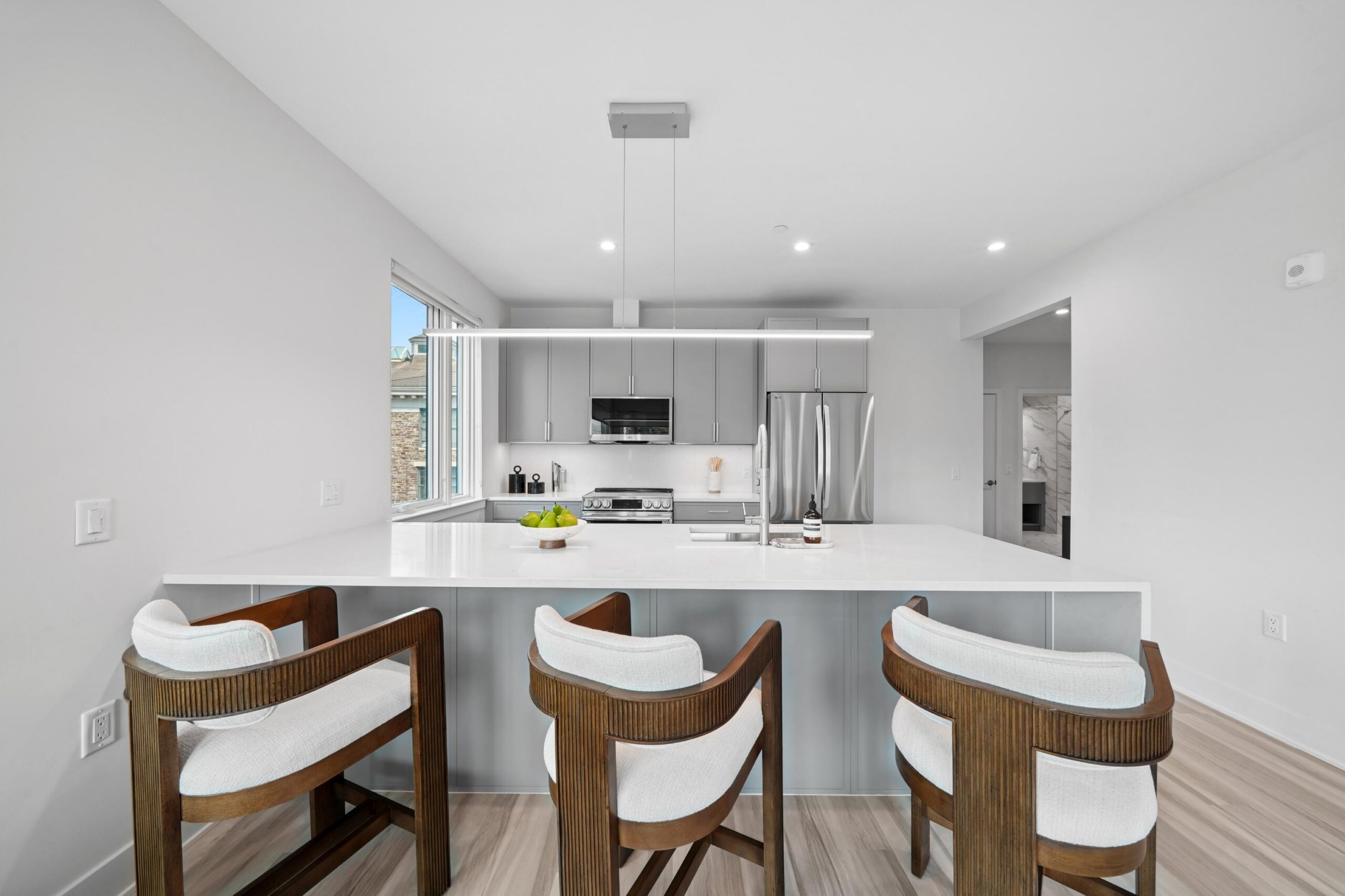 Kitchen area with grey cabinets and while details. 3 bar stools by kitchen island